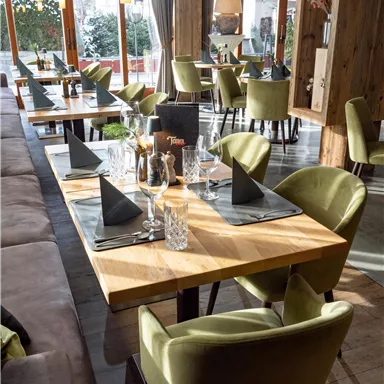A modern restaurant with bright tables and stylish green chairs. The tables are elegantly set and provide an inviting atmosphere.