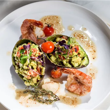An elegant dish with stuffed avocados, shrimp, and a cherry tomato. The food is creatively presented and garnished with herbs.