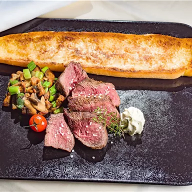 A gourmet dish with tender beef, sautéed vegetables, and a large piece of bread. The meal is accompanied by fresh herbs and a sauce.