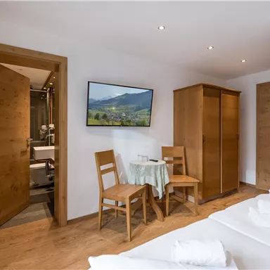 A modern room with hardwood flooring and cozy furnishings. A table with two chairs and a beautiful view of the mountains through a picture on the wall.