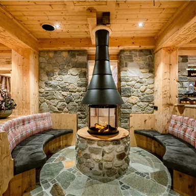 Ein gemütlicher Wohnbereich mit einem modernen Kamin und Holzverkleidung. Die Bänke sind mit weichen Kissen ausgestattet und schaffen eine einladende Atmosphäre.