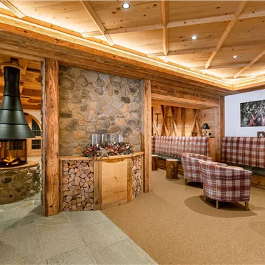 Ein gemütlicher Innenraum mit Holzverkleidung und einem modernen Kamin. Bequeme Sessel und eine warme Atmosphäre laden zum Entspannen ein.