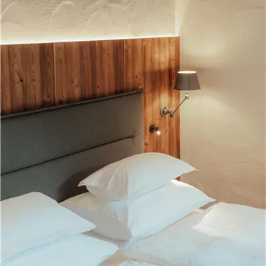 A modern bedroom with a comfortable double bed and soft pillows. On the wall, there is a wooden panel and a stylish wall lamp.