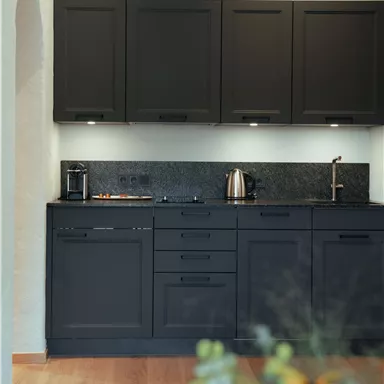 A modern kitchen with black cabinets and an elegant countertop. The equipment includes a coffee maker, a kettle, and a stove.