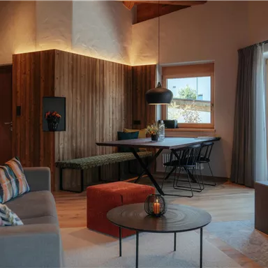 A modern living room with a cozy couch and a dining table. The wood paneling and soft lighting create an inviting atmosphere.
