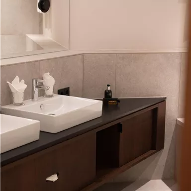 A modern bathroom with double sinks and an elegant wooden cabinet. The walls are in neutral colors, and there is subtle lighting.