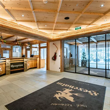 Eine einladende Hotellobby mit einer Rezeption aus Holz und modernen Glaswänden. Weihnachtsdekorationen verleihen dem Raum eine gemütliche Atmosphäre.