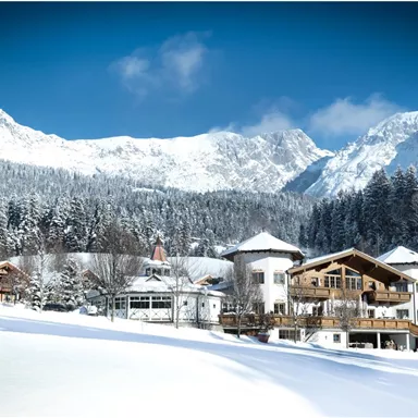 Eine malerische Winterlandschaft mit schneebedeckten Bergen und traditionellen Chalets. Der blaue Himmel und die klare Luft schaffen eine friedliche Atmosphäre.