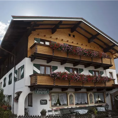 Ein charmantes, traditionelles Haus mit Holzverkleidung und blühenden Balkonen. Die Umgebung ist grün und malerisch, ideal für einen Urlaub in den Bergen.