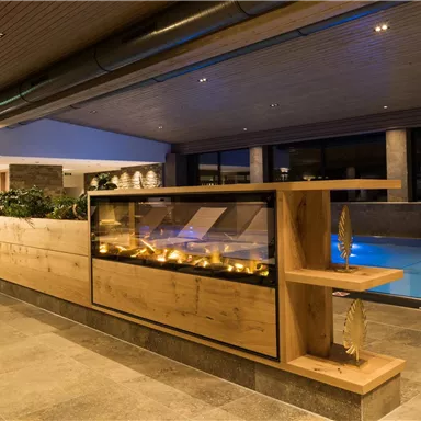 An elegant interior with a wooden shelf and a decorative display case. In the background, a lit swimming pool creates a relaxing atmosphere.