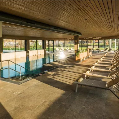 An elegant indoor pool area with loungers and large windows. The atmosphere is bright and inviting, perfect for relaxation.