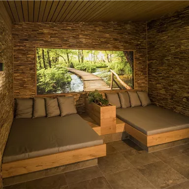 A cozy room with two loungers and a natural stone wall. A large picture of a forest path completes the relaxed atmosphere.