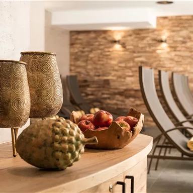 A stylish room with a wooden cabinet, decorative vases, and a fruit bowl. In the background, comfortable lounges can be seen.