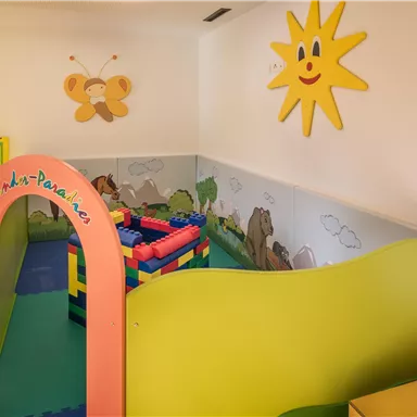 A colorful play area for children with a play mat and building blocks. On the wall, there's a cheerful sun and animal motifs.