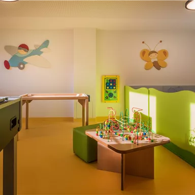 A bright playroom with colorful walls and games for children. There is a toy landscape, tables and chairs, as well as a foosball table.