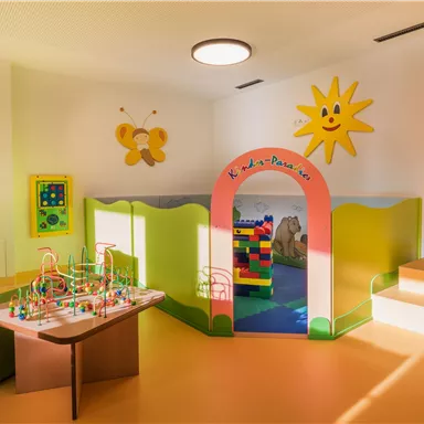A bright and cheerful playroom for children with colorful toys and a play castle. The walls are designed in cheerful colors, and the room is well-lit.