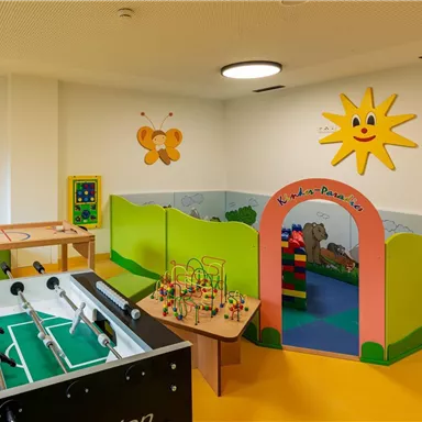 A colorful playroom for children with a table football game and a play area. Cheerful decorations such as airplanes, flowers, and a sun are attached to the walls.