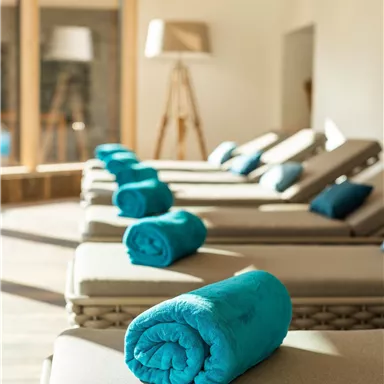 A relaxing wellness area with loungers and colorful towels. The large windows let in plenty of light.