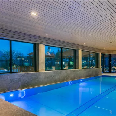 A stylish swimming pool with blue water and large windows. The modern interior design offers a view of the surrounding landscape.