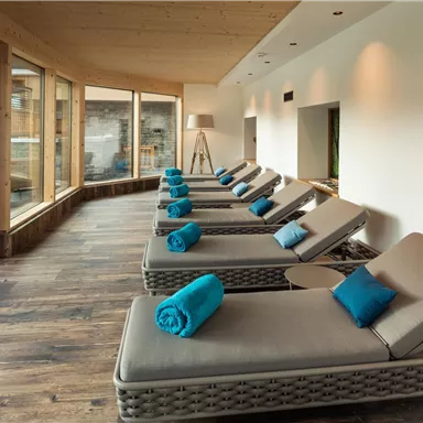A quiet relaxation area with loungers and blue towels. Large windows offer views of nature.