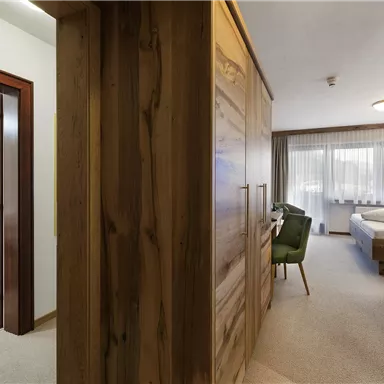 A bright room with a comfortable bed and a cozy seating area. The walls are neutrally painted and the window provides plenty of daylight.