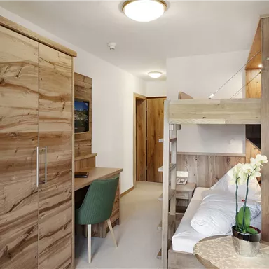 A modern room with wooden furniture and a cozy atmosphere. There is a bunk bed, a desk, and a stylish plant.