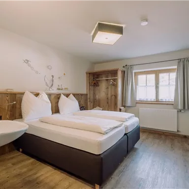 Ein gemütliches Zimmer mit zwei Einzelbetten und Holzelementen. Großes Fenster mit Blick nach draußen und hellen Vorhängen.