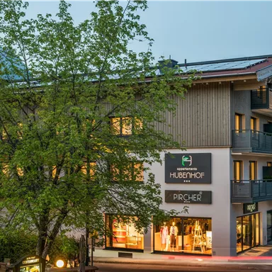 A modern building with beautiful wood design and large windows. Trees surround the house and gently illuminate the surroundings.