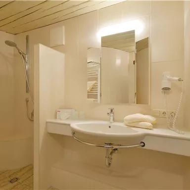 Ein modernes Badezimmer mit einer Dusche und einem Waschbecken. Die Wände sind hell gehalten und es gibt frische Handtücher.