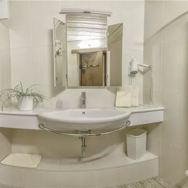 Ein modernes Badezimmer mit einem Waschbecken, Spiegel und Handtuchhaltern. Die sanften Farben und die Pflanzen sorgen für eine einladende Atmosphäre.