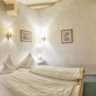 Ein gemütliches Schlafzimmer mit einem großen Bett und sanfter Beleuchtung. Auf der linken Seite befindet sich eine Treppe, die zu einer oberen Etage führt.
