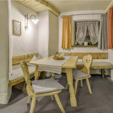 Ein gemütlicher Essbereich mit Holzstuhl und Tisch. Die Wände sind in hellem Weiß gehalten, und die Fenster sind mit Vorhängen dekoriert.