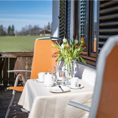 Ein schöner Balkon mit einem Tisch, der für ein Frühstück gedeckt ist. Auf dem Tisch stehen Blumen, Geschirr und Gläser.