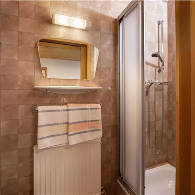 Ein Badezimmer mit einer Dusche, einem Spiegel und einem Handtuchhalter. Die Wände sind mit quadratischen Fliesen in neutralen Farben gestaltet.