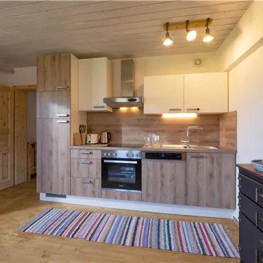 Eine moderne Küche mit Holzschränken und einem Herd. Der Boden ist mit einem bunten Teppich bedeckt.