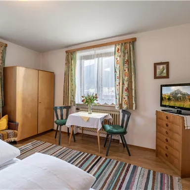 Ein gemütliches Schlafzimmer mit zwei Betten und einem kleinen Sitzbereich. Das Zimmer ist hell und freundlich eingerichtet, mit einem Fenster und einem Fernseher.