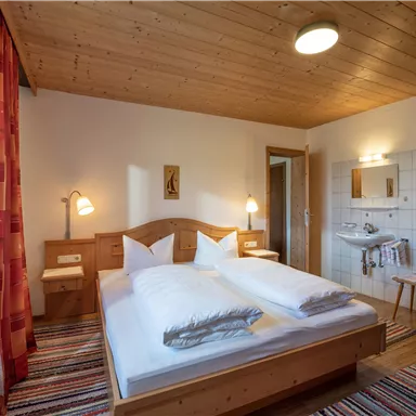 Ein gemütliches Schlafzimmer mit einem Doppelbett und Holzdekor. Licht und freundliche Farben schaffen eine einladende Atmosphäre.