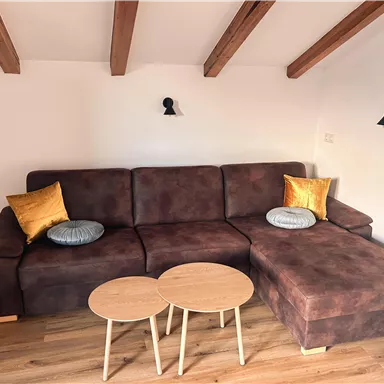 Eine gemütliche Sitzecke mit einem braunen Sofa und dekorativen Kissen. Dazu gehören auch zwei kleine Tischchen aus Holz, alles in einem hellen, modernen Raum.