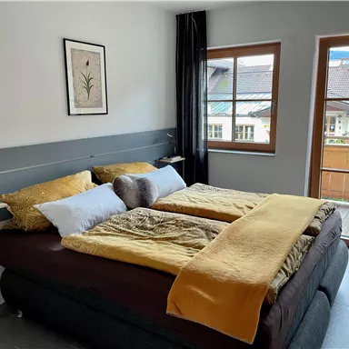 A cozy bedroom with a large bed and warm colors. There is a window overlooking a balcony and the surrounding buildings.