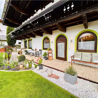Ein gemütliches Haus mit einem gepflegten Garten. Der Außenbereich ist mit bunten Blumen und Sitzgelegenheiten ausgestattet.