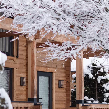 Ein gemütliches Holzhaus im Schnee. Die Bäume sind mit einer weißen Schneedecke bedeckt.