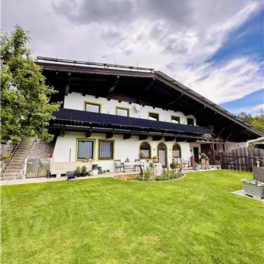 Ein traditionelles Haus mit einem großen Garten und vielen Pflanzen. Der Himmel ist bewölkt und es gibt einen Hauch von blauem Himmel.