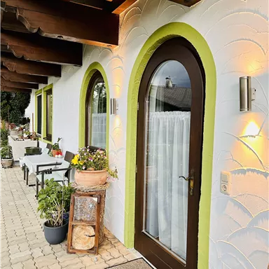 Ein schöner Eingang mit einem braunen Tor und grünen Akzenten. Vor der Tür stehen Pflanzen und Tische, die eine einladende Atmosphäre schaffen.