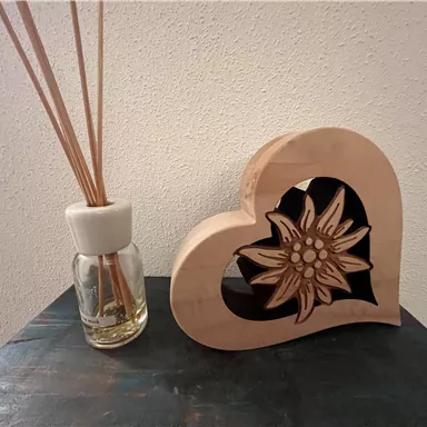 A wooden heart with a flower inside stands next to a scent container with long sticks. The scene conveys a cozy and decorative atmosphere.