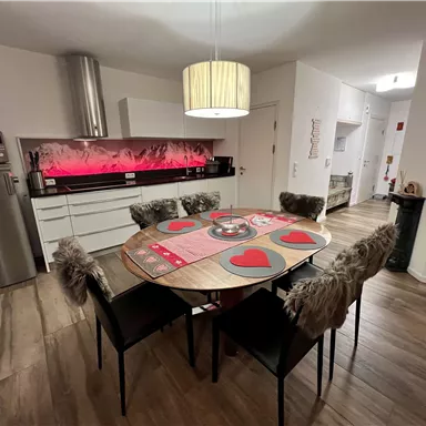 A modern kitchen with a round table and chairs. The walls are bright, and warm light creates an inviting atmosphere.