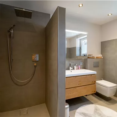 Ein modernes Badezimmer mit einer Dusche und einer Holzwaschtisch. Die Wände sind in neutralen Grautönen gehalten und die Beleuchtung ist angenehm.