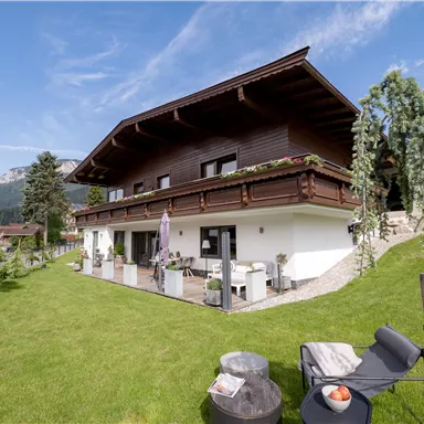 Ein modernes Haus im alpinen Stil mit einem großen Garten. Der klare Himmel und die umliegende Landschaft bieten eine entspannte Atmosphäre.