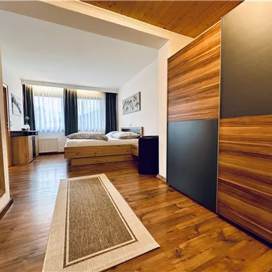 Ein modernes Zimmer mit zwei Betten und einem großen Spiegel. Die Holzböden und Fenster sorgen für eine angenehme Atmosphäre.