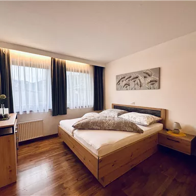 Ein modernes Schlafzimmer mit einem Doppelbett und Holzverkleidung. Große Fenster lassen viel Tageslicht herein.