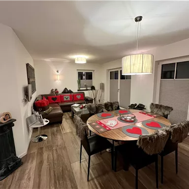 A modern living room with a round table and chairs. The table is decorated with red hearts, while the walls are bright and inviting.